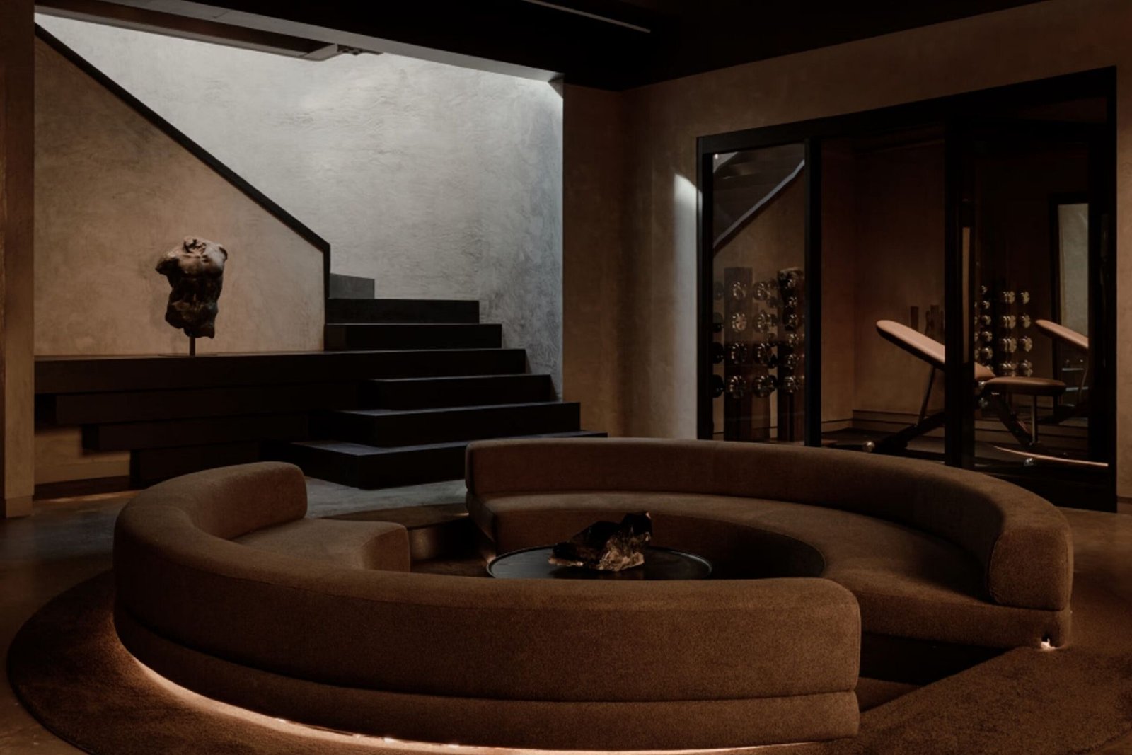 Remedy Place circular sunken lounge sofa beside glass-walled fitness rooms and a sculptural staircase