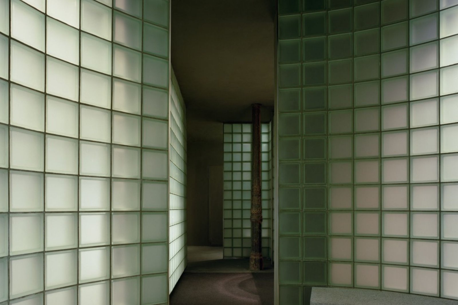 Riela Madrid curved seafoam glass-block walls framing a dark interior with a cast-iron column