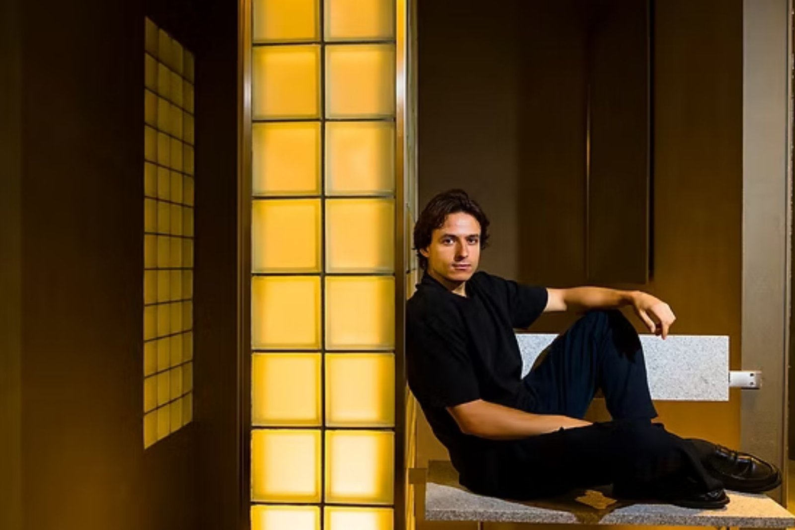 The Riela Madrid founder seated on a stone bench before a glowing amber glass-block wall
