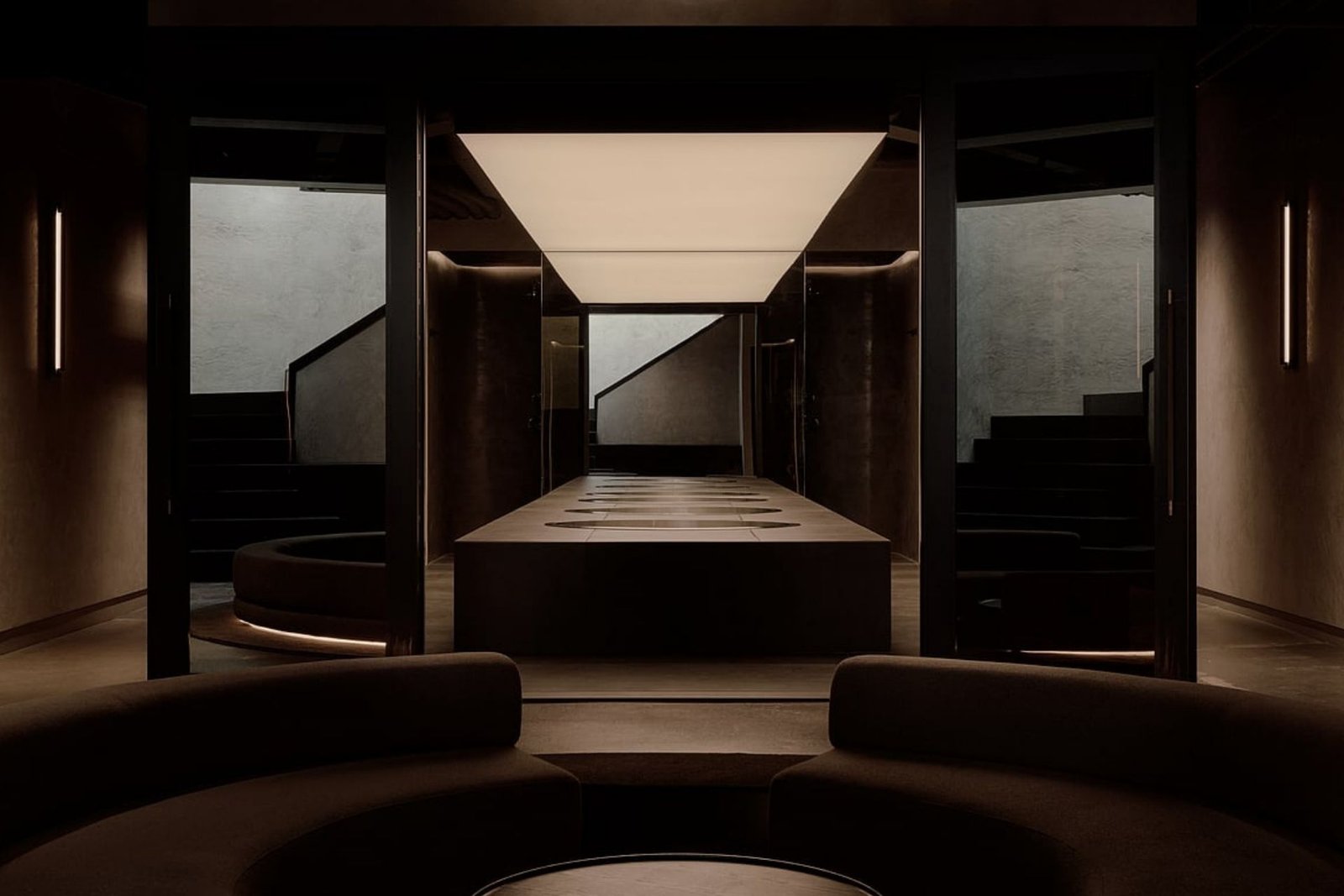 Remedy Place lounge curving towards a glass-walled hydrotherapy space with a glowing ceiling and cold plunge