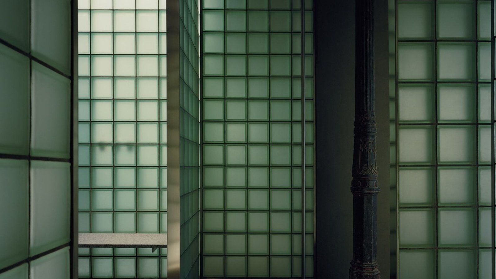 Layered green glass-block partitions and a Victorian cast-iron column at Riela Madrid