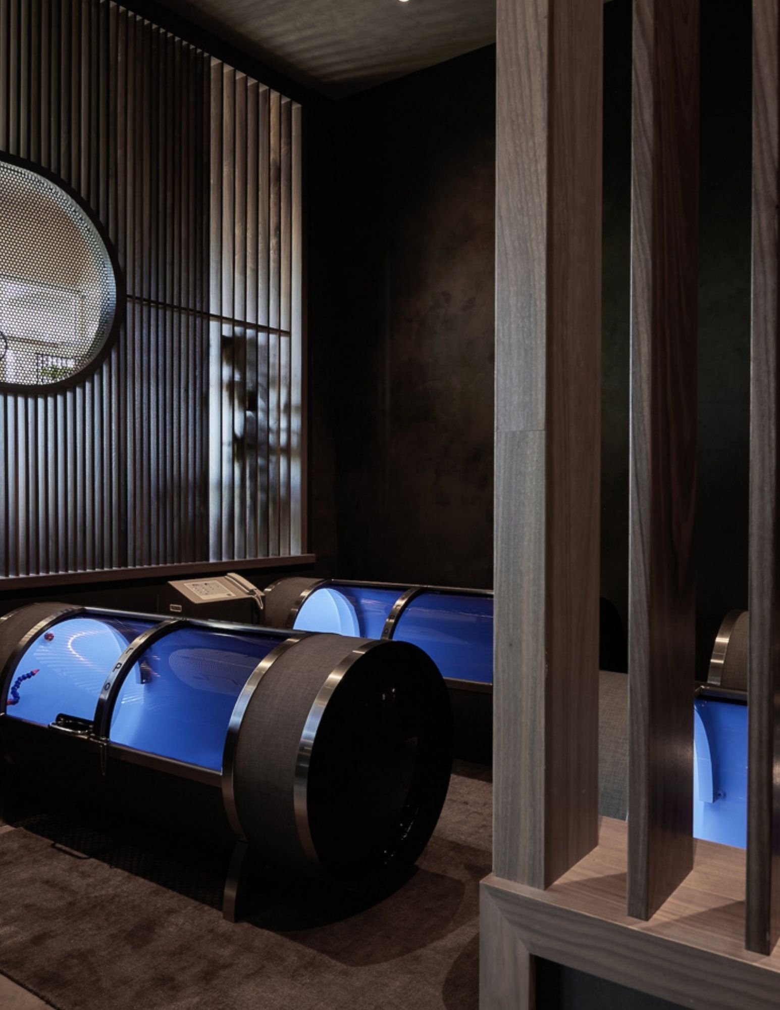 Remedy Place flotation pods glowing blue in a wood-clad sensory-deprivation room