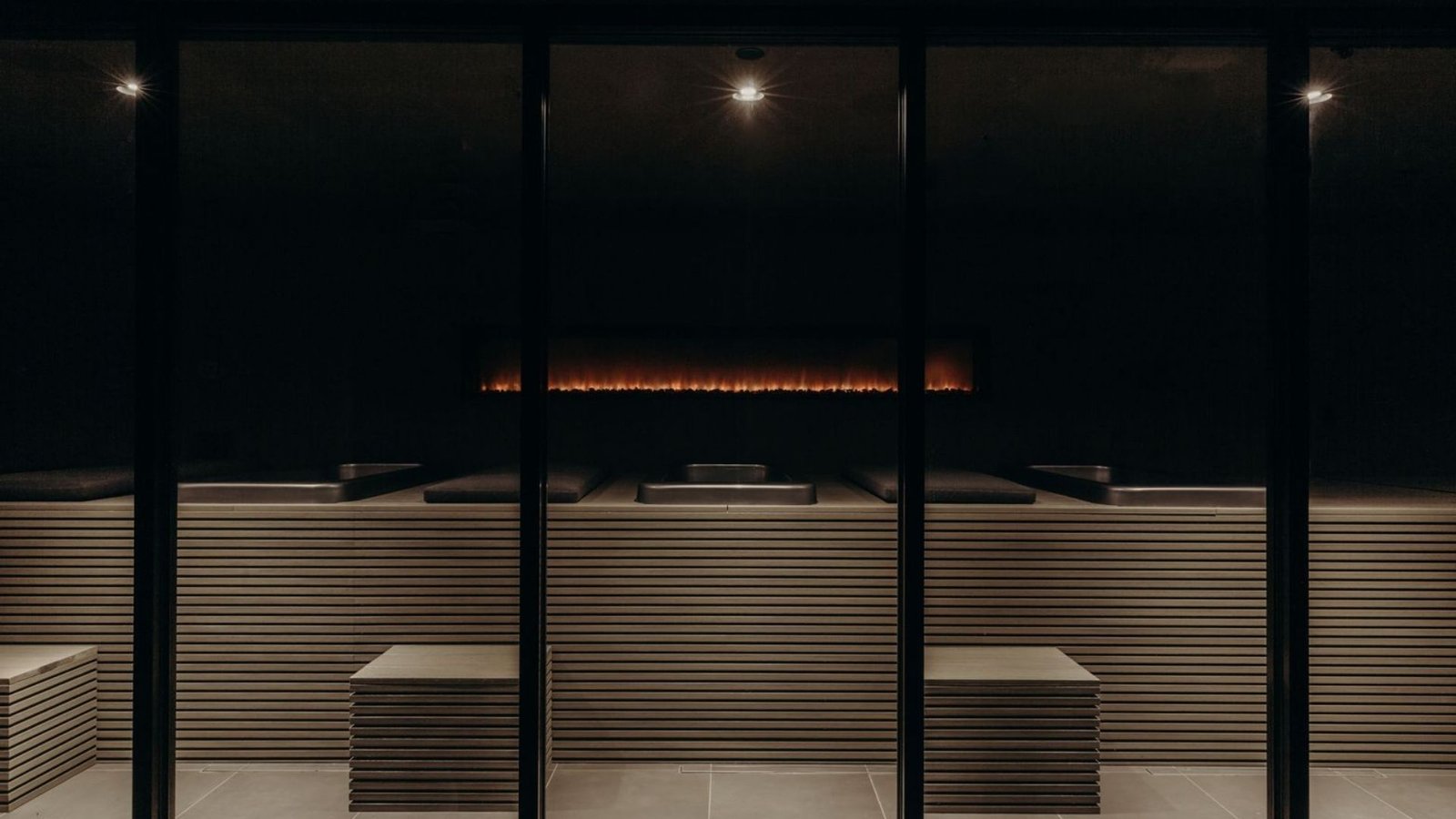Remedy Place communal sauna room centred on a long linear fireplace with shared bench seating