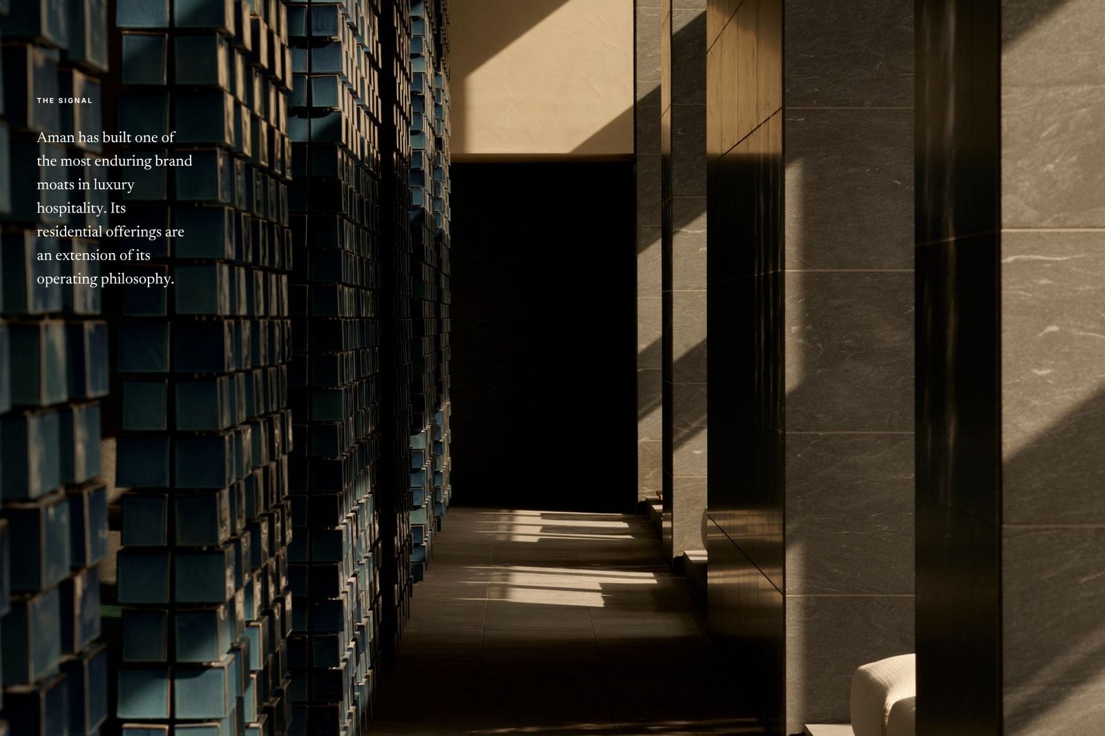 A sunlit interior corridor at an Aman property, with deep blue hand-glazed tiled columns beside dark stone walls, overlaid with Edition Media's 'The Signal' caption on Aman's brand moat.