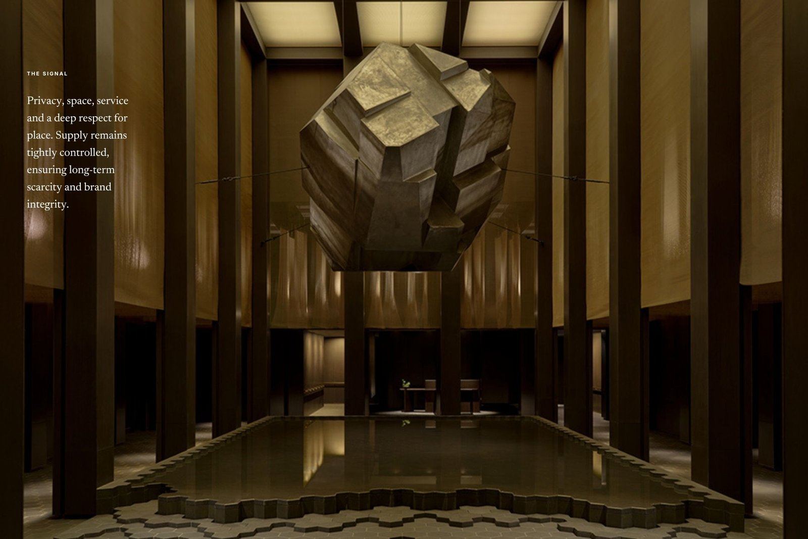 An Aman lobby with a floating gilded sculpture hovering above a mirror-quiet reflecting pool, framed by dark timber columns and warm golden walls, with an Edition Media 'The Signal' caption on scarcity.