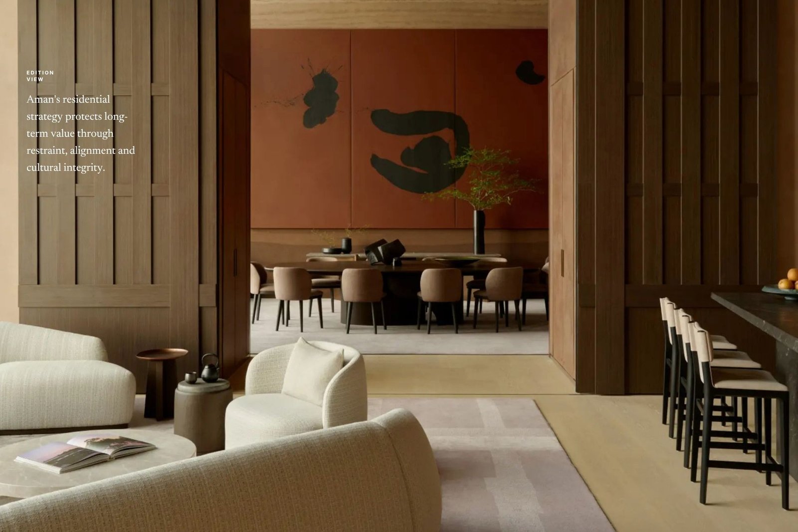 An Aman residence living and dining space in warm woods, cream boucle seating, a terracotta ink-brush artwork and a bar counter, overlaid with Edition Media's 'Edition View' caption on long-term value.