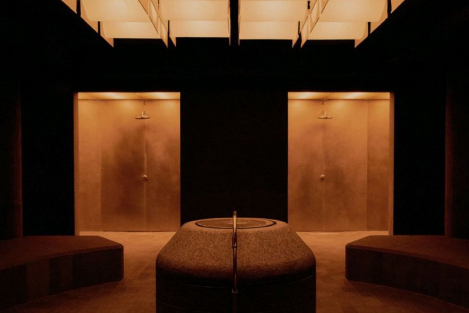The Altar's thermal steam room, with a luminous coffered ceiling, twin shower alcoves, a central stone basin and curved benches in warm amber light.