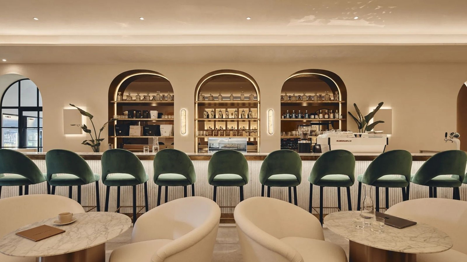 Saint Haven cafe and lounge bar behind backlit arched shelving, emerald stools